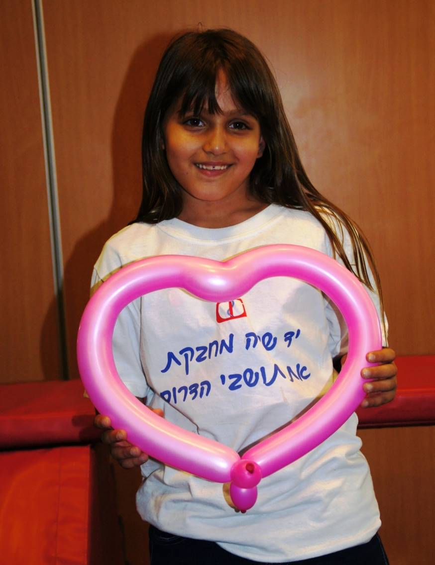 A young girl stands holding a heart shaped balloon. She is wearing a Yad Sarah sweatshirt. This is a good day because this Ashkelon girl has a reprieve from the scud missiles for a day of fun at Yad Sarah.