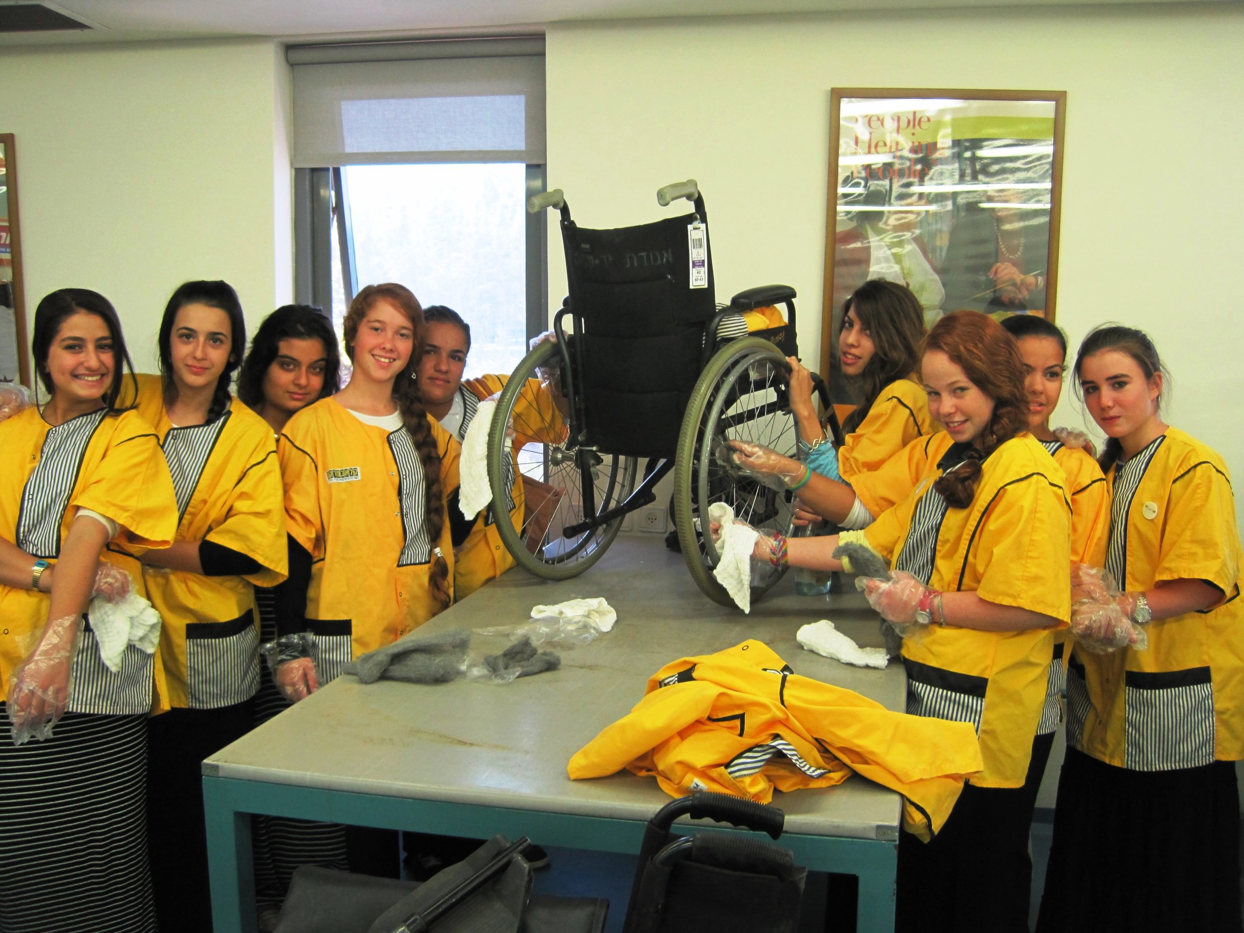 Students at the Visitors' Center in bright yellow aprons learn how to clean wheelchairs after they are returned to Yad Sarah