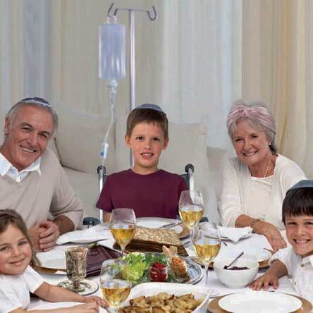 A smiling Jewish family sitting at a holiday table. A young boy sitting in a wheelchair at the head of the table.