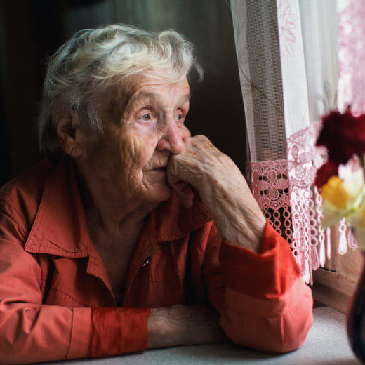 Older woman looks out window. Loneliness and fear are constant in her life.