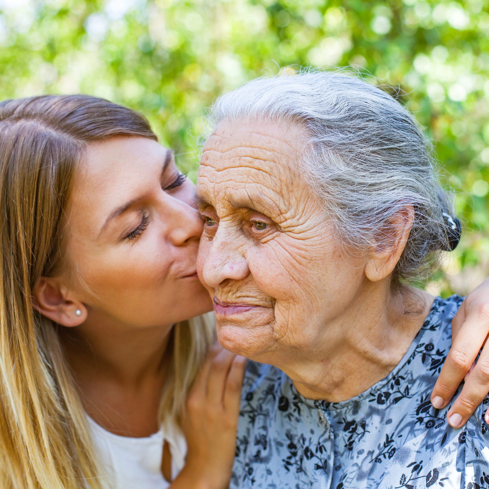 Young woman kissing her old grandmother in the park