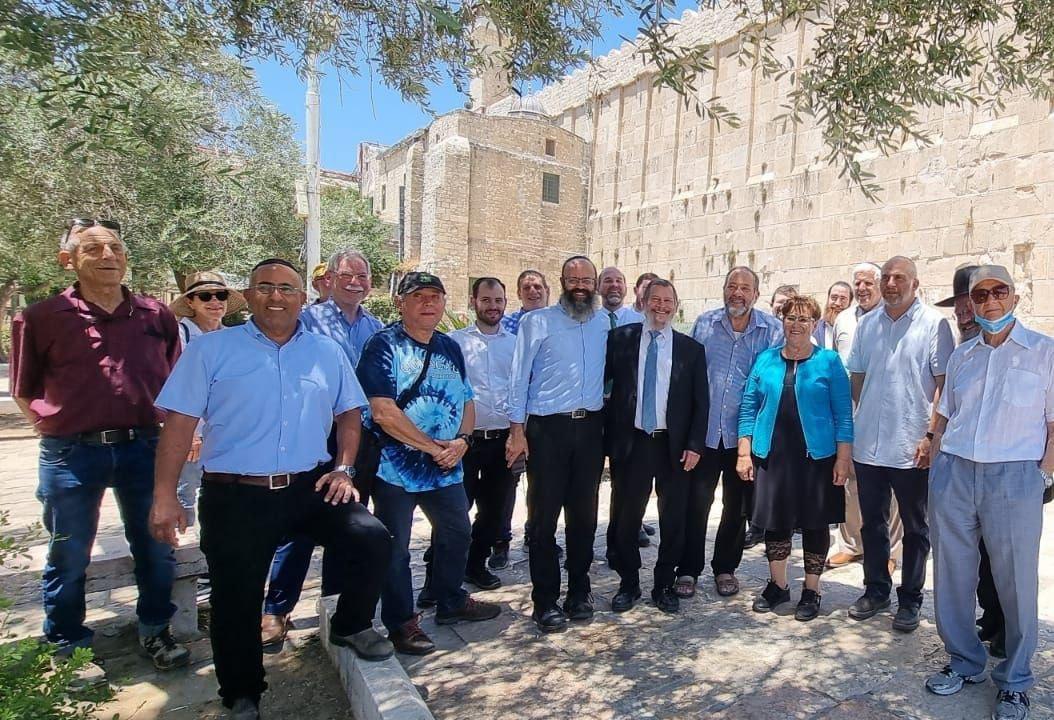 Group of Men and Women standing in the shade of a tree in front of a branch of Yad Sarah in Southern Israel